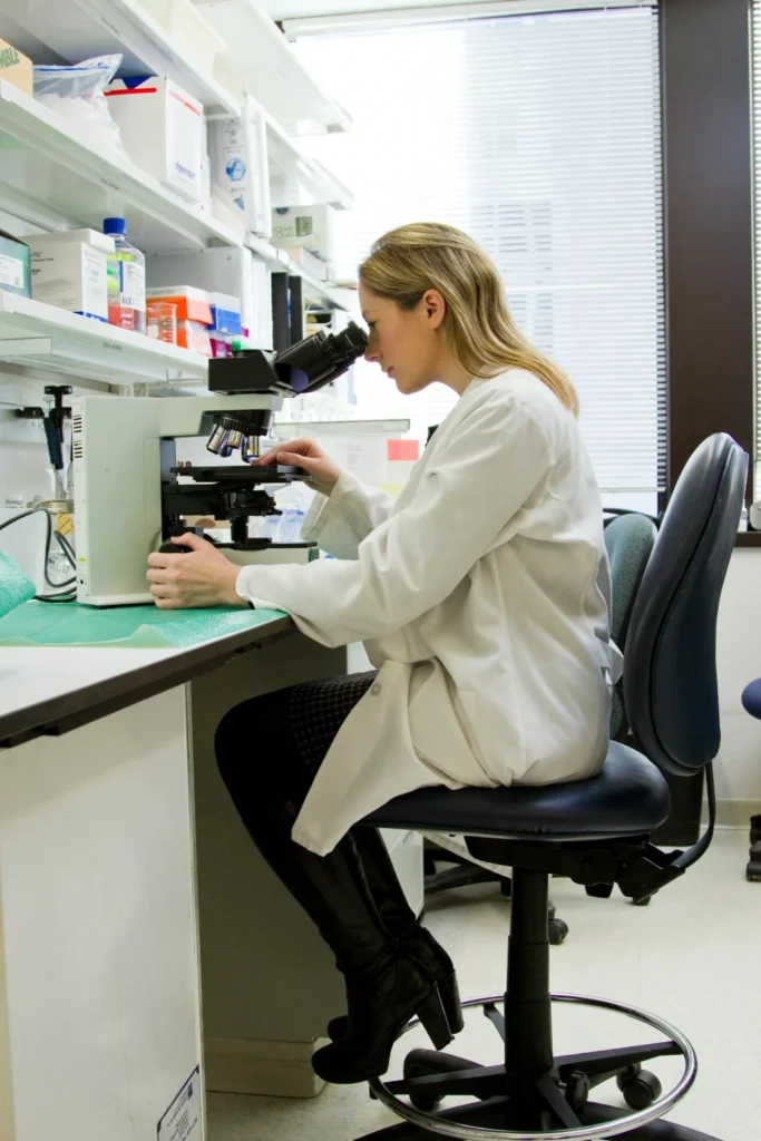 woman in a lab coat in a lab looking into a microscope.